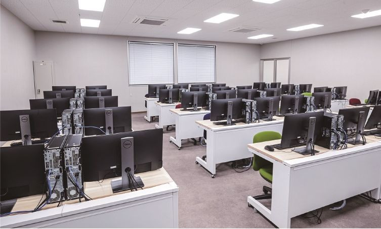 写真：106実習室。机がたくさん並んでおり、机の上にはパソコンとモニターが置かれている。