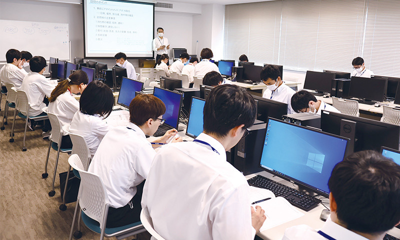 写真：職業専門実践課程の企業連携授業の様子。教室で学生たちがパソコンに向かい作業をしている。