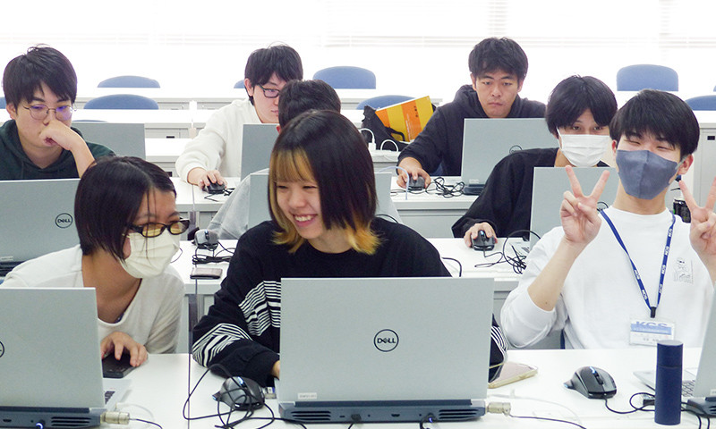 写真：プログラミングバトルの様子。数人の学生がノートパソコンへ向かい作業をしている。