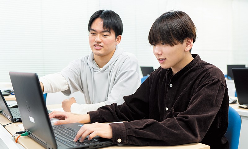 写真：隣の学生と話しながらノートパソコンで作業をしている光永さん