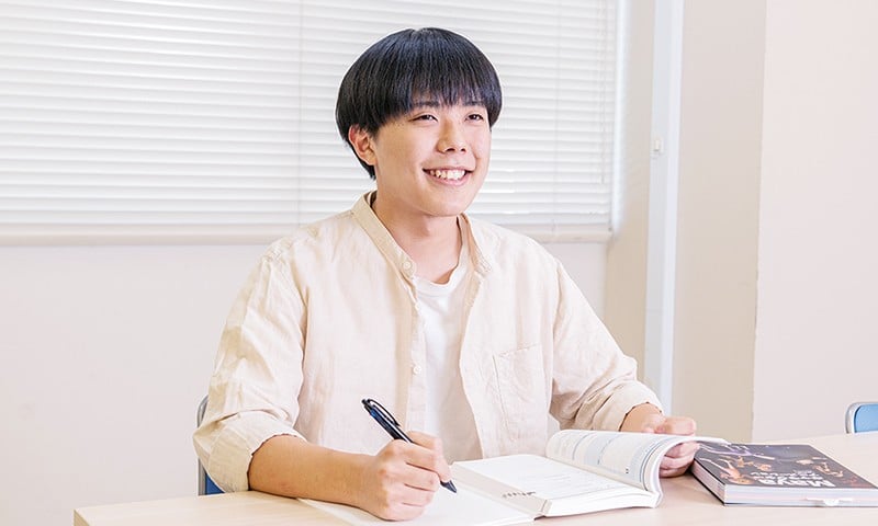 写真：机でテキストとノートを広げ、楽しそうに勉強をしてい