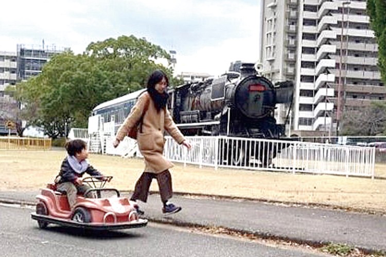 写真：カートに乗った香川先生の子どもと、その隣を歩く香川先生。写真奥側にはSLが見える。
