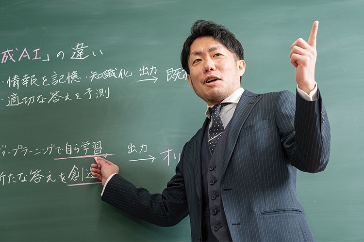 写真：スーツを着た男性。黒板の前に立ち、AIについて熱心に教えている。