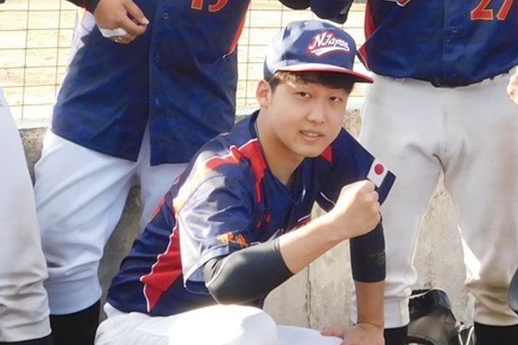写真：草野球チームのユニフォームを着て、ポーズを取っている今井先生。