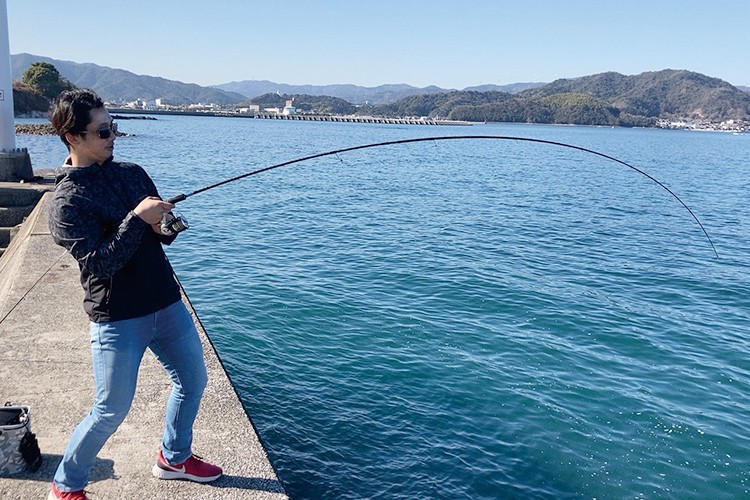 写真：サングラスを掛け、海釣りをしている稗田先生。手に持った竿がしなっている。