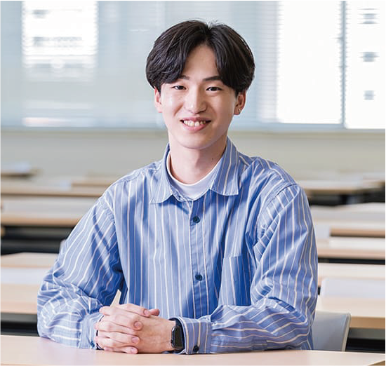 写真：青と白の縦ストライプ柄のシャツを着た笑顔の男子学生。