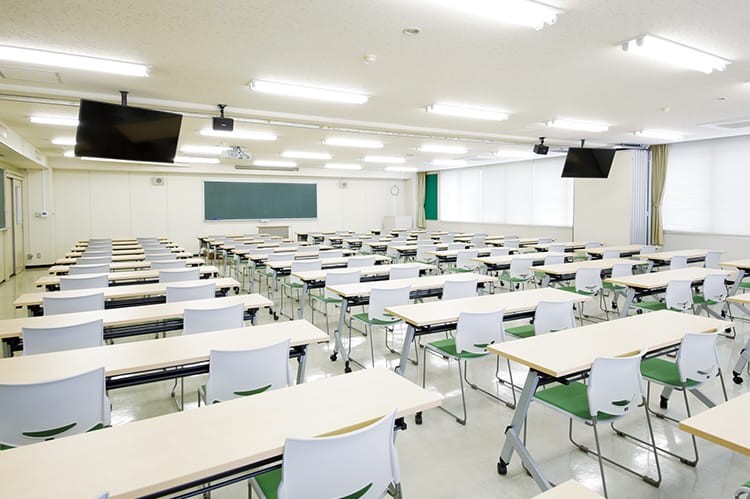 写真：座学教室。明るい雰囲気の教室に2人掛けの机がたくさん並んでいる。