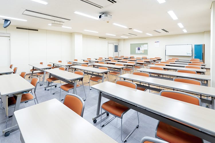 写真：座学教室。明るい雰囲気の教室に2人掛けの机がたくさん並んでいる。