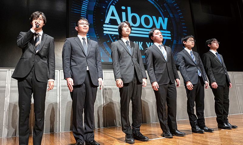写真：卒業研究発表会の様子。女子学生が壇上に立ち発表している。