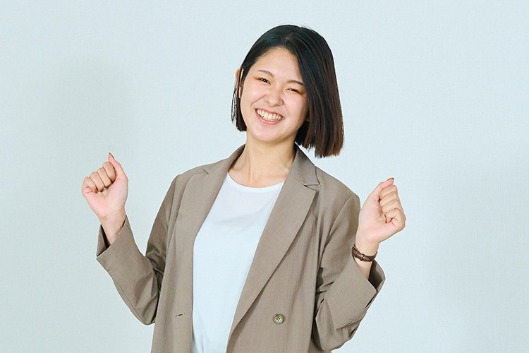 画像：ショートヘアの女性が明るく笑顔でポーズを取っている。彼女は両手を軽く上げて楽しそうな雰囲気を表現している。