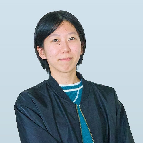 写真：黒いジャケットを着た女性学生。淡いブルーの背景の前で、静かにカメラを見つめている。