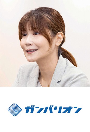 写真：グレージュ色のスーツを着た、穏やかな表情の女性。 ロゴ：ガンバリオン