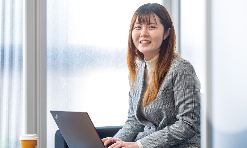写真：スーツを着た微笑んでいる女性。後ろの壁にMICのロゴマークが掲げられている。