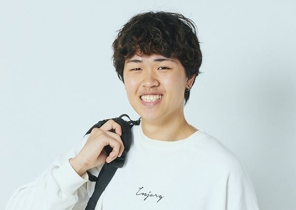 写真：グレーのスウェットを着た男子学生。スマートフォンで電話をかけている。